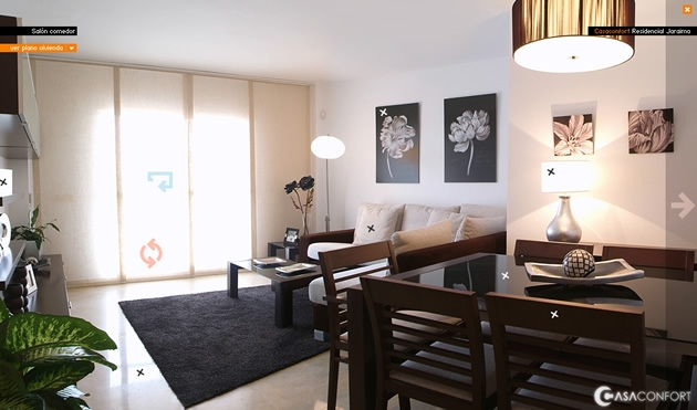 Foto panorámica del salon-comedor de un piso piloto de Casaconfort. Las flechas que se ven sobre la foto permiten navegar a otras estancias del piso. 